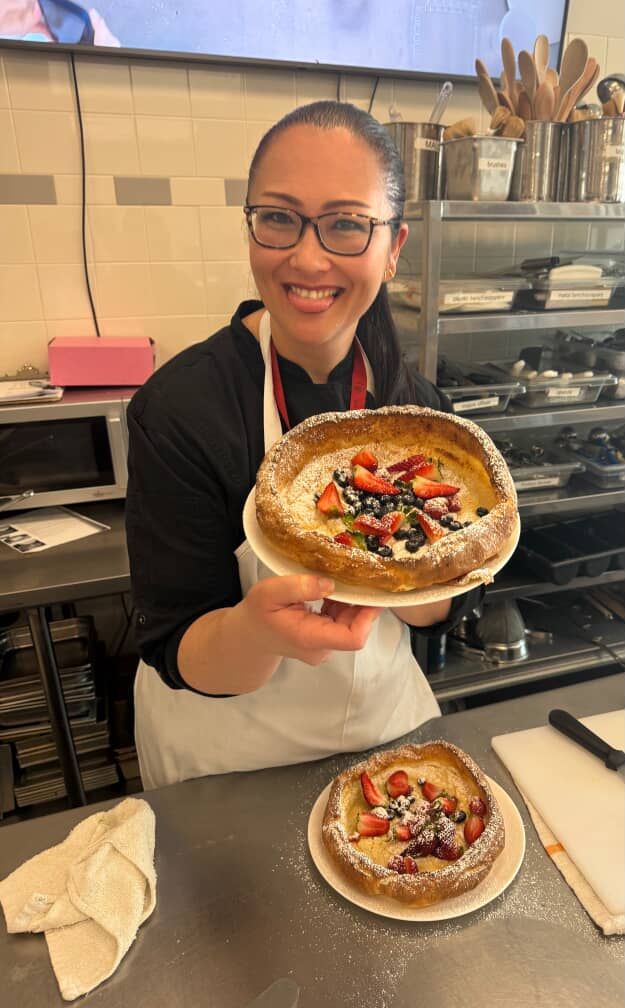 Chef  Kristianne Descher, standing in the kitchen, holding pastry, and smiling