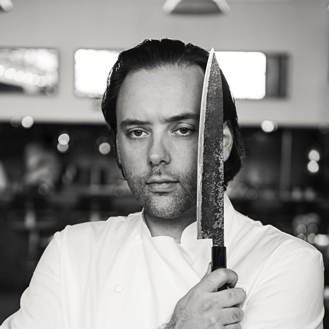Chef Paul Liebrandt in a black & white photo holding a knife in the kitchen