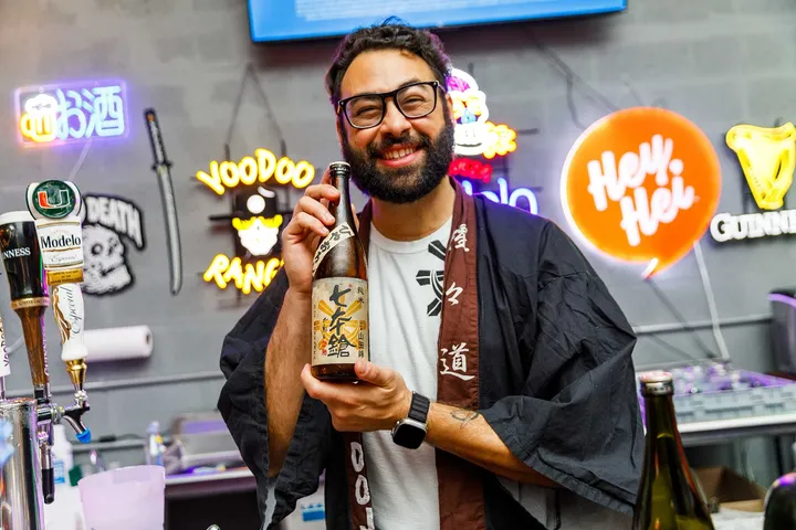 Haidar Hachem holding a bottle of sake and smiling to the camera