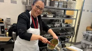 Chef  Kristianne Descher wearing an apron, standing in a kitchen, holding pastry in her hands, and smiling