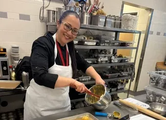 Chef  Kristianne Descher wearing an apron, standing in a kitchen, holding pastry in her hands, and smiling