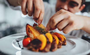 A plate with a fancy dish and a blurry chef in the background