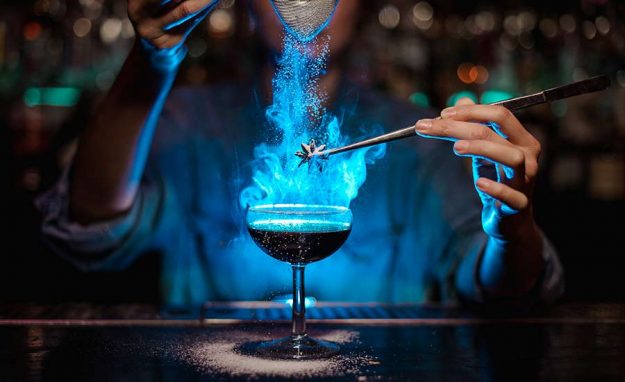 A woman bartender makes fancy, bright blue cocktail