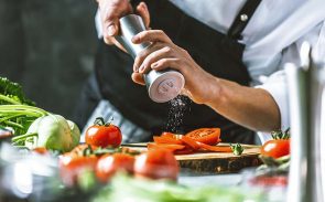 A cook is grinding salt above a wooden cutting board with sliced tomatoes.
