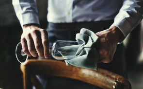 A male fine dining server's hand wiping a wine glass with a cloth