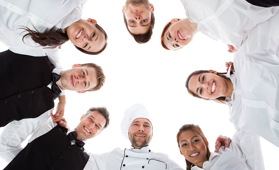 A group of different kinds of restaurant staff huddled together and looking down with the camera from the ground up.