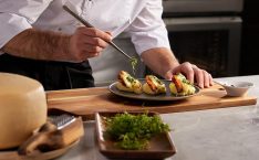 Cook interview questions: A male cook is finishing up a delicious-looking dish on a plate, on a wooden board.