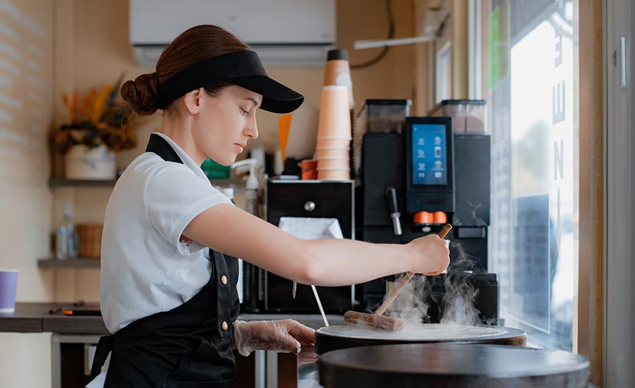 Fast-food job description: a young woman inn uniform is making a pancake in a fast-food place.