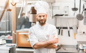 Line cook job description: a confident, smiling male cook in uniform is standing in a restaurant kitchen.