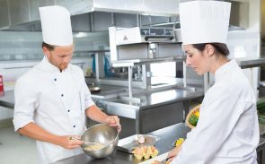 Earning their line cook salary, a male and a female cook are preparing a meal in a restaurant kitchen.