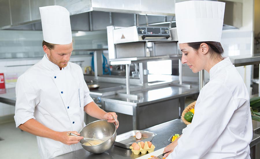 Earning their line cook salary, a male and a female cook are preparing a meal in a restaurant kitchen.
