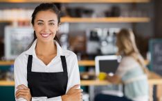 Waitress interview questions: A smiling waitress in a coffee place, wearing an apron.