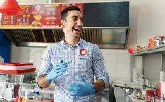 Young adult Caucasian fast food worker standing and smiling while having fun at work and wearing protective medical gloves