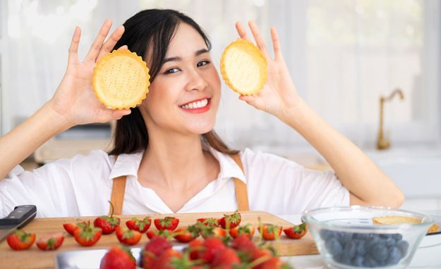 A female pastry chef smiling and holding two pieces of pastry on each of her hand