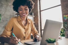 A girl smiling in front of a laptop while writing