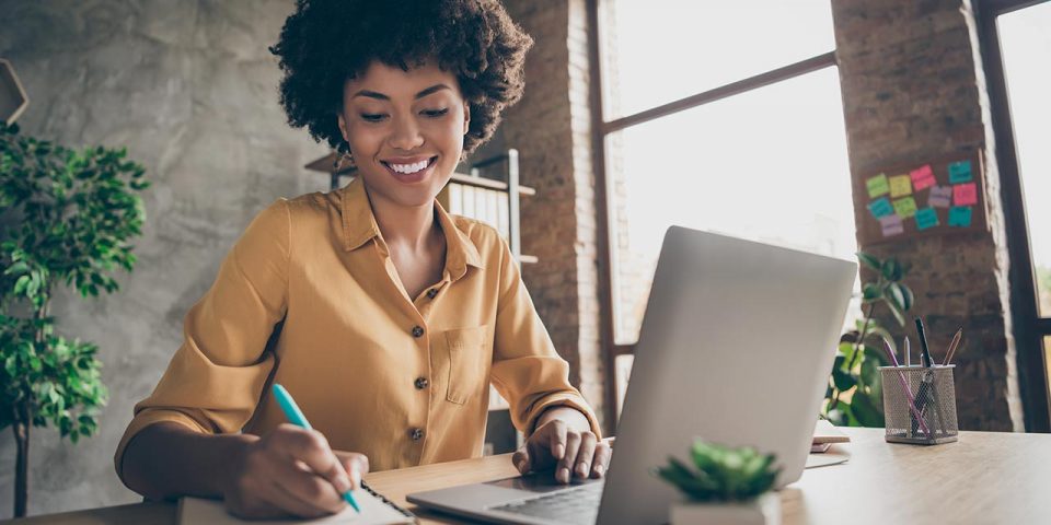 A girl smiling in front of a laptop while writing