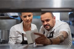 A male food expeditor and a female kitchen manager discussing a customer's order on a sheet of paper