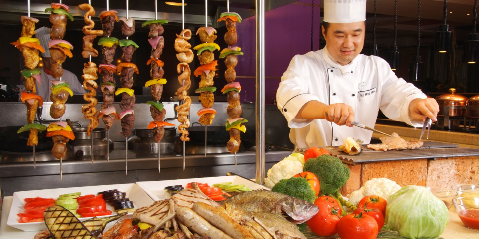 A man preparing meat and vegetables on a grill