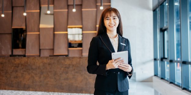 A female Asian hotel manager smiling and holding a tablet