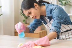 A female maid with gloves on cleaning a countertop with a rag