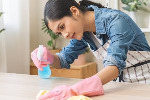 A female Maid with gloves on cleaning a countertop with a rag