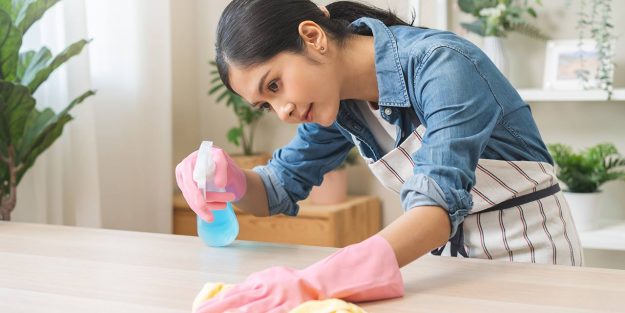 A female maid with gloves on cleaning a countertop with a rag