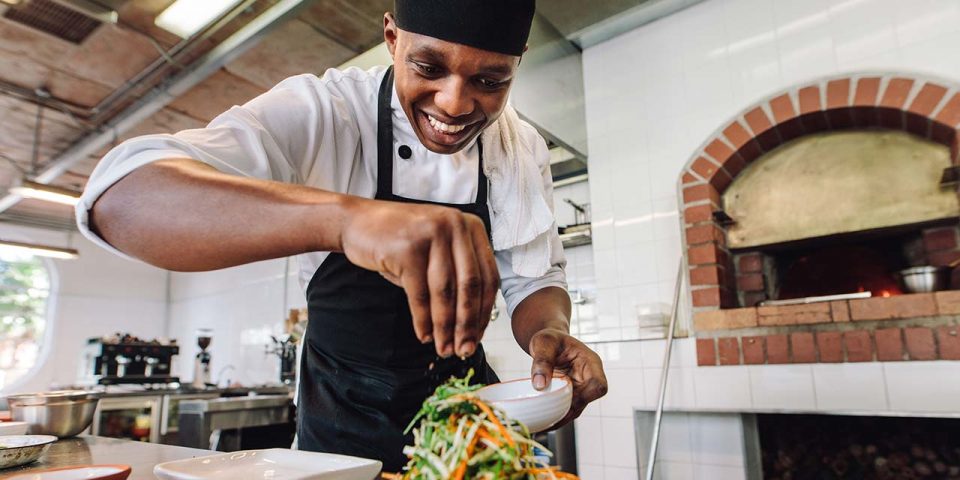 a smiling pantry chef seasoning the salad