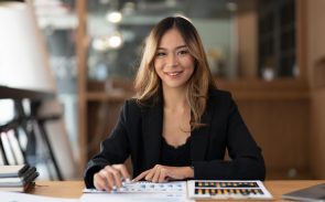 A female Asian payroll analyst smiling with her right hand on the desk