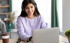 A female community manager smiling and wearing headphones while working with her laptop