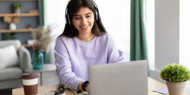 A female community manager smiling and wearing headphones while working with her laptop