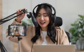 A female content creator wearing headphones and sitting in front of a phone camera