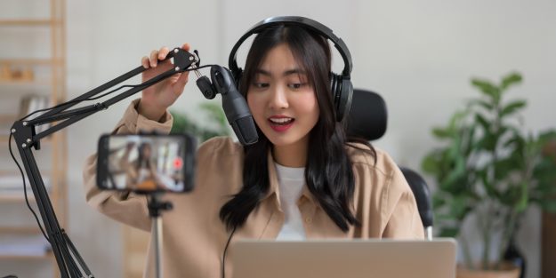 A female content creator wearing headphones and sitting in front of a phone camera
