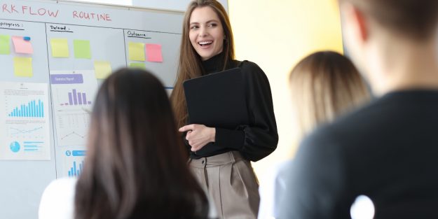 A female job coach standing in front of a class of job seekers with a whiteboard behind her