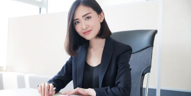 A woman sales coordinator wearing professional attire and sitting on her desk