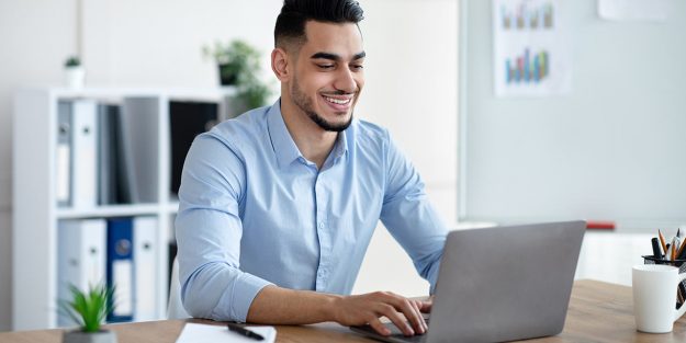 A male employee smiling while typing on his laptop