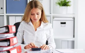 A female long-haired tax preparer using her calculator with documents on her desk