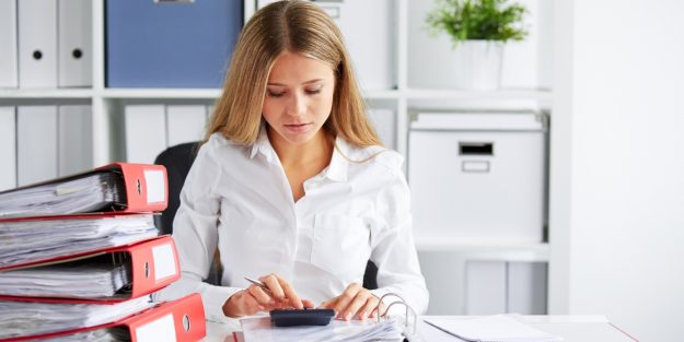 A female long-haired tax preparer using her calculator with documents on her desk