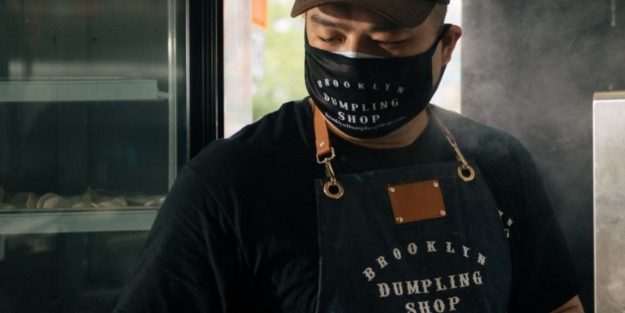 A chef from Brooklyn Dumpling Shop wearing a face mask and a cap