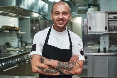 Young chef crossing his arms and standing in front of the kitchen