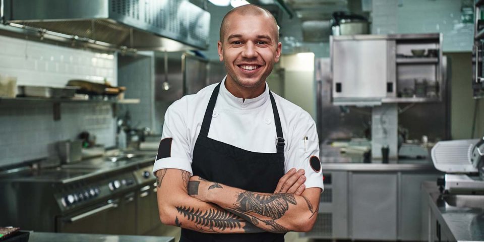 Young chef crossing his arms and standing in front of the kitchen