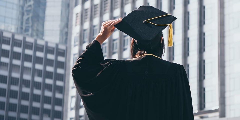 Back view of a woman in graduation attire holding her cap