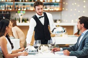 Young server in an upscale restaurant serving a couple