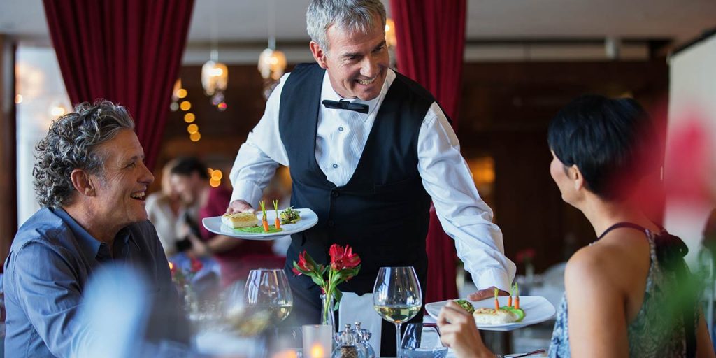 A fine-dining waiter bringing plates to clients