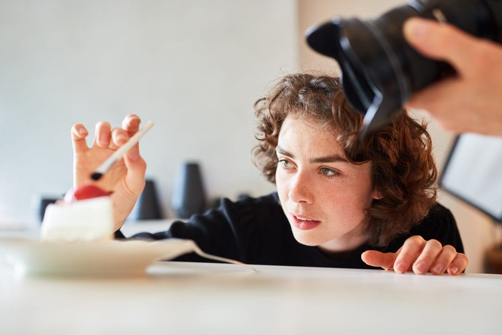 Curly-haired, female Food Stylist adding final touches to a cake