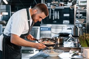 A male Chef wearing an apron and plating his dish; how chefs find inspiration