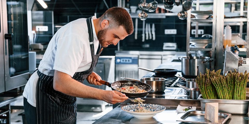 A male Chef wearing an apron and plating his dish; how chefs find inspiration