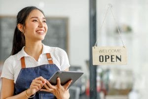 A restaurant employee holding a tablet and smiling in front of an open sign