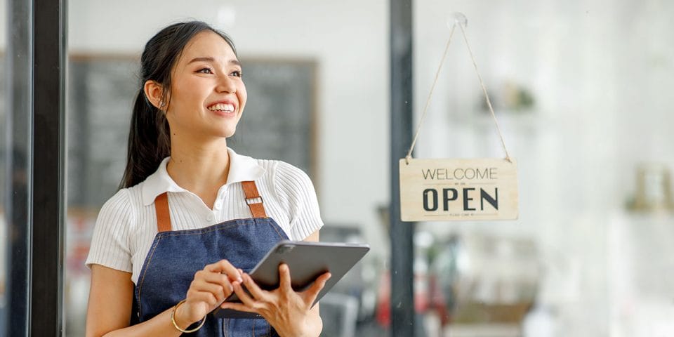 A restaurant employee holding a tablet and smiling in front of an open sign