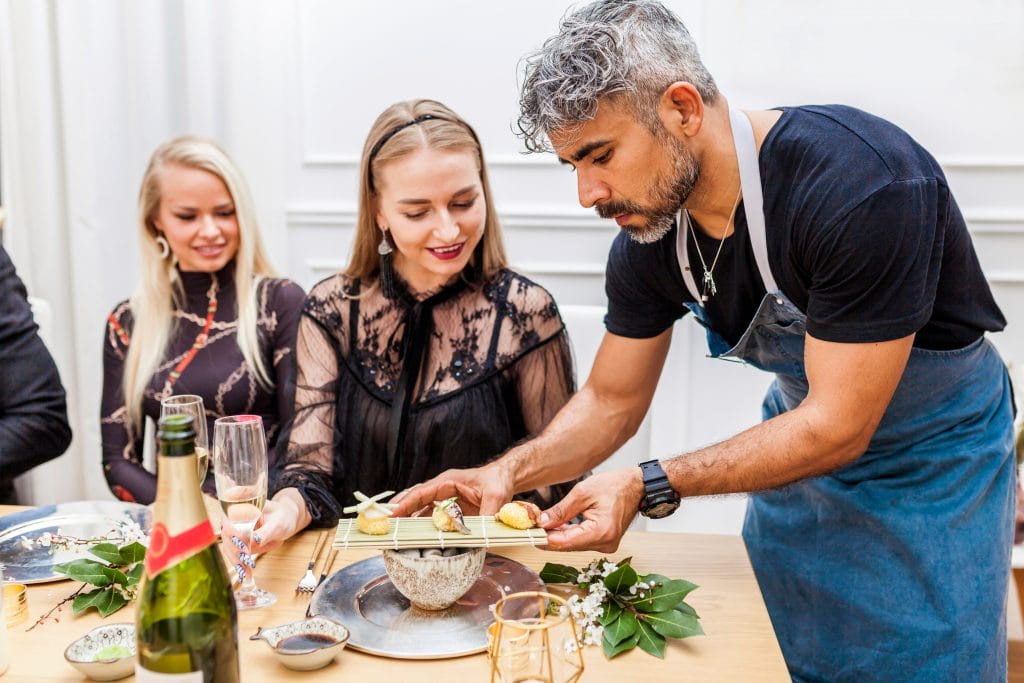 A male Private Chef serving a dish to his client and guests