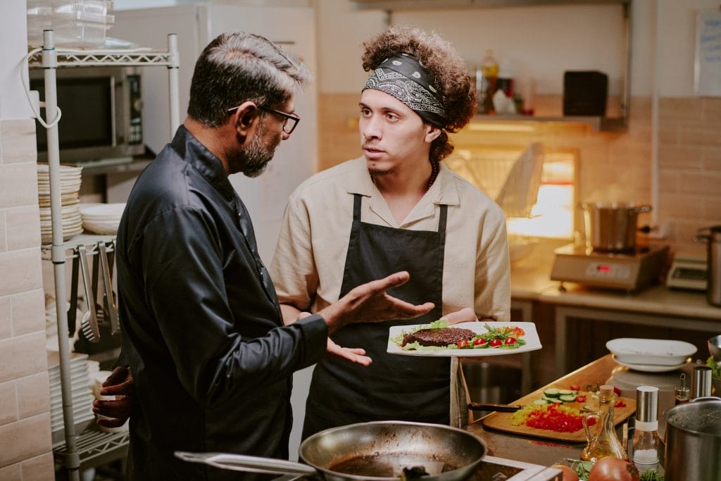 A male Sous Chef discussing a dish with a male Executive Chef